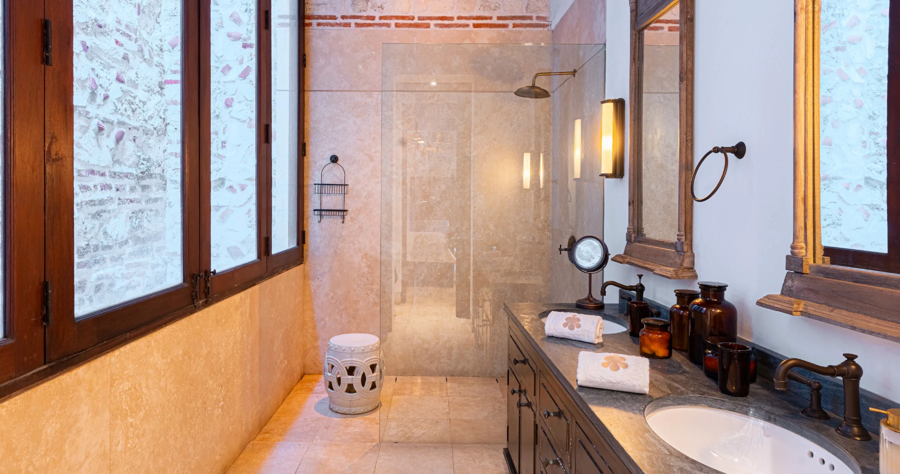 Baño privado de diseño contemporáneo con doble lavabo sobre encimera de madera, espejos redondos modernos y acabados en piedra