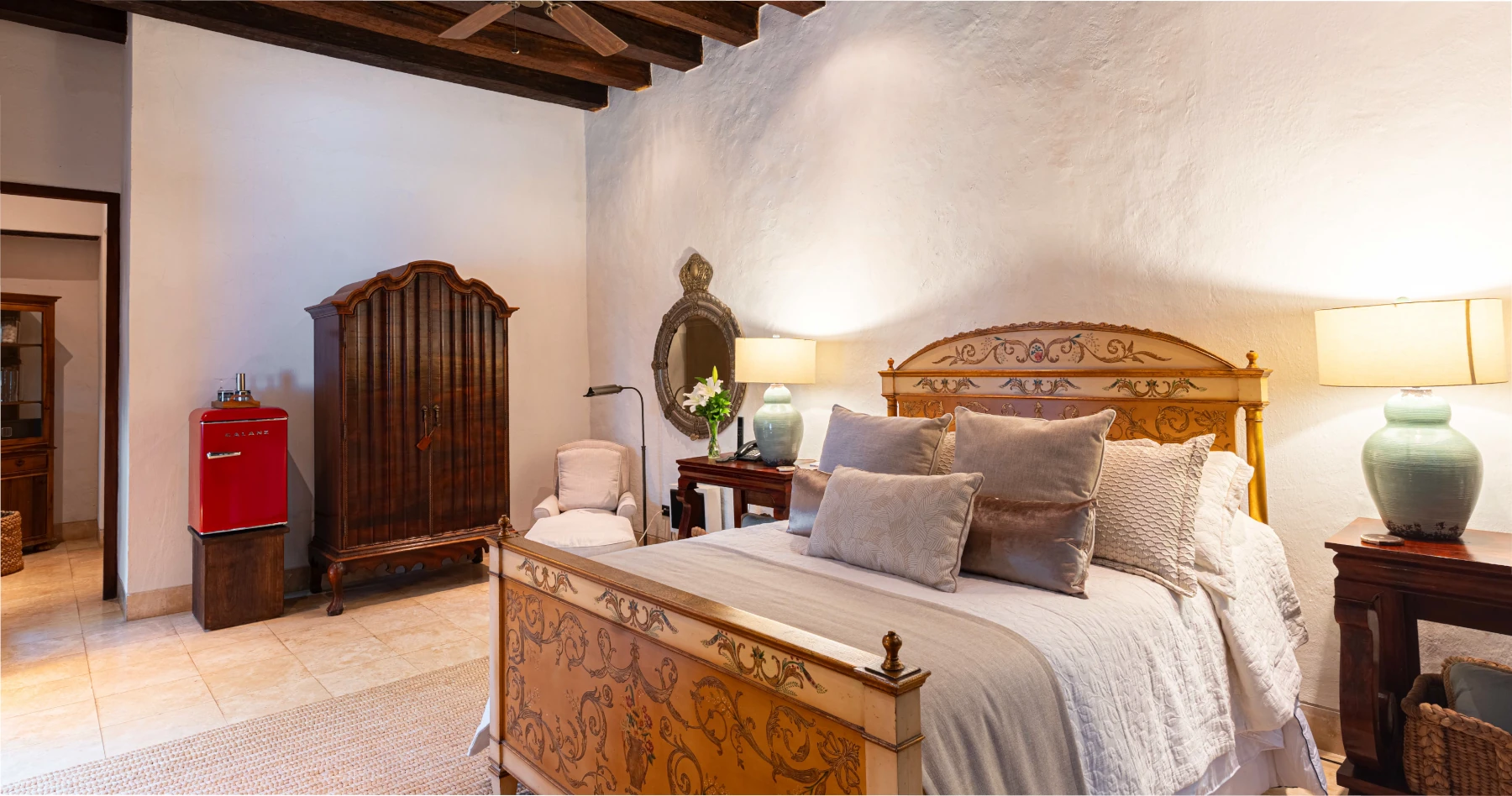 Detalle de la suite Coral con techos altos de vigas de madera, iluminación perimetral moderna y ventanales tradicionales de madera tallada