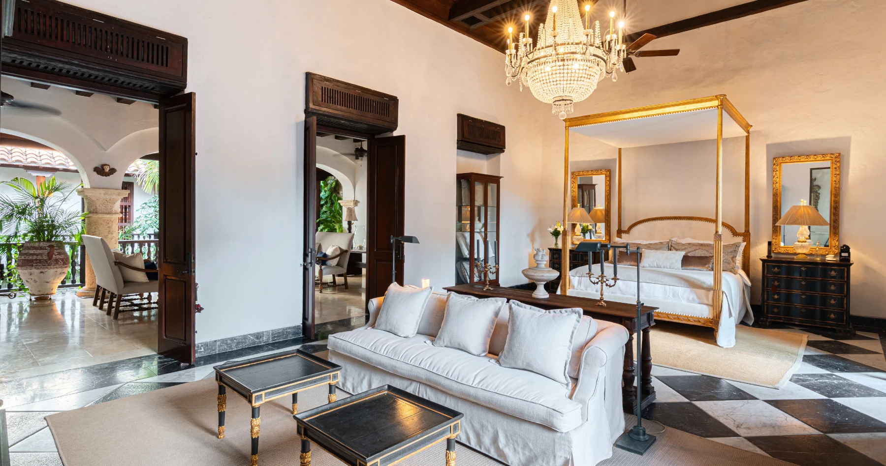 Detalle de suite colonial con mobiliario de madera fina, iluminación cálida y acceso a balcón privado con puertas tradicionales