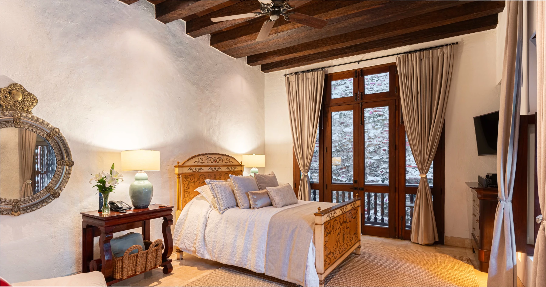 Dormitorio de lujo con cama King, textiles premium en tonos tierra y una impresionante pared de piedra original que resalta el carácter colonial