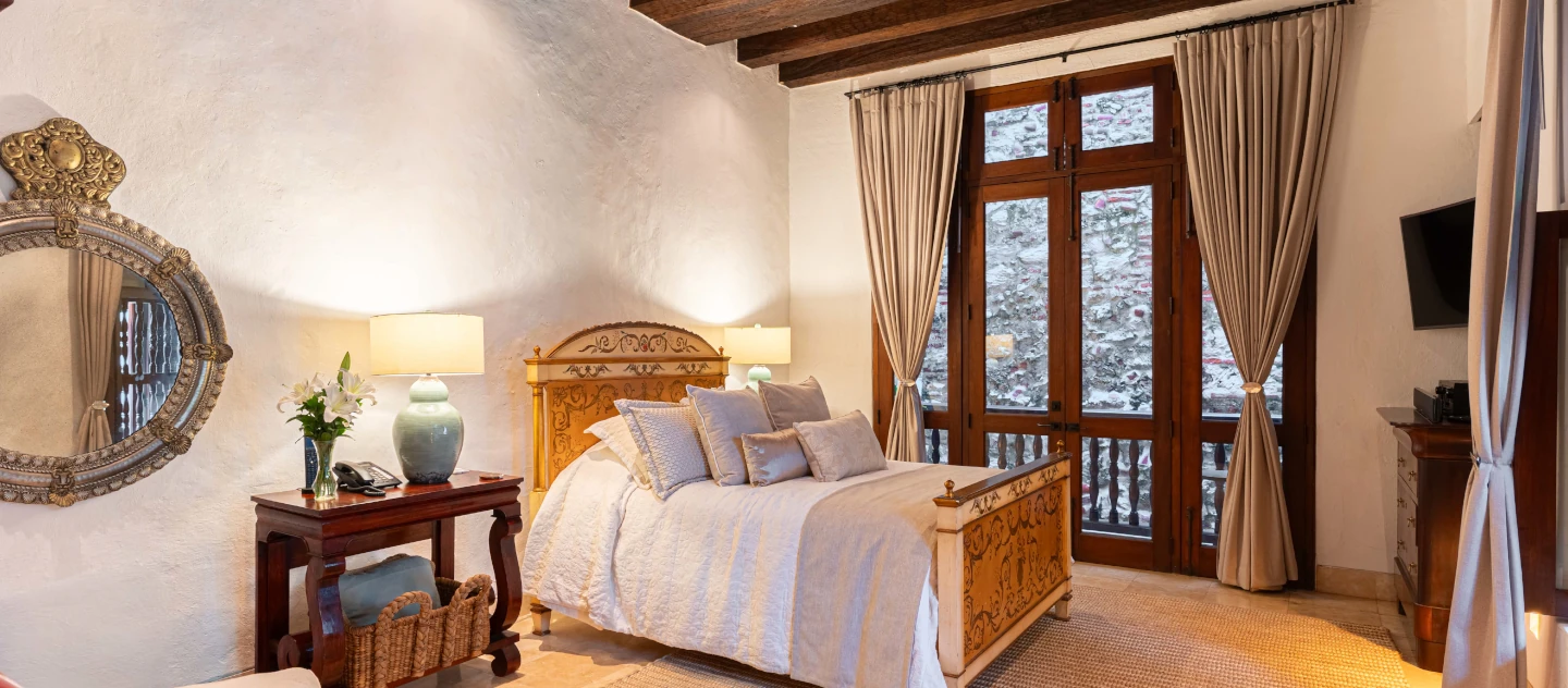 Habitación boutique con decoración colonial, vigas de madera, espejos ornamentales y amplios ventanales de madera