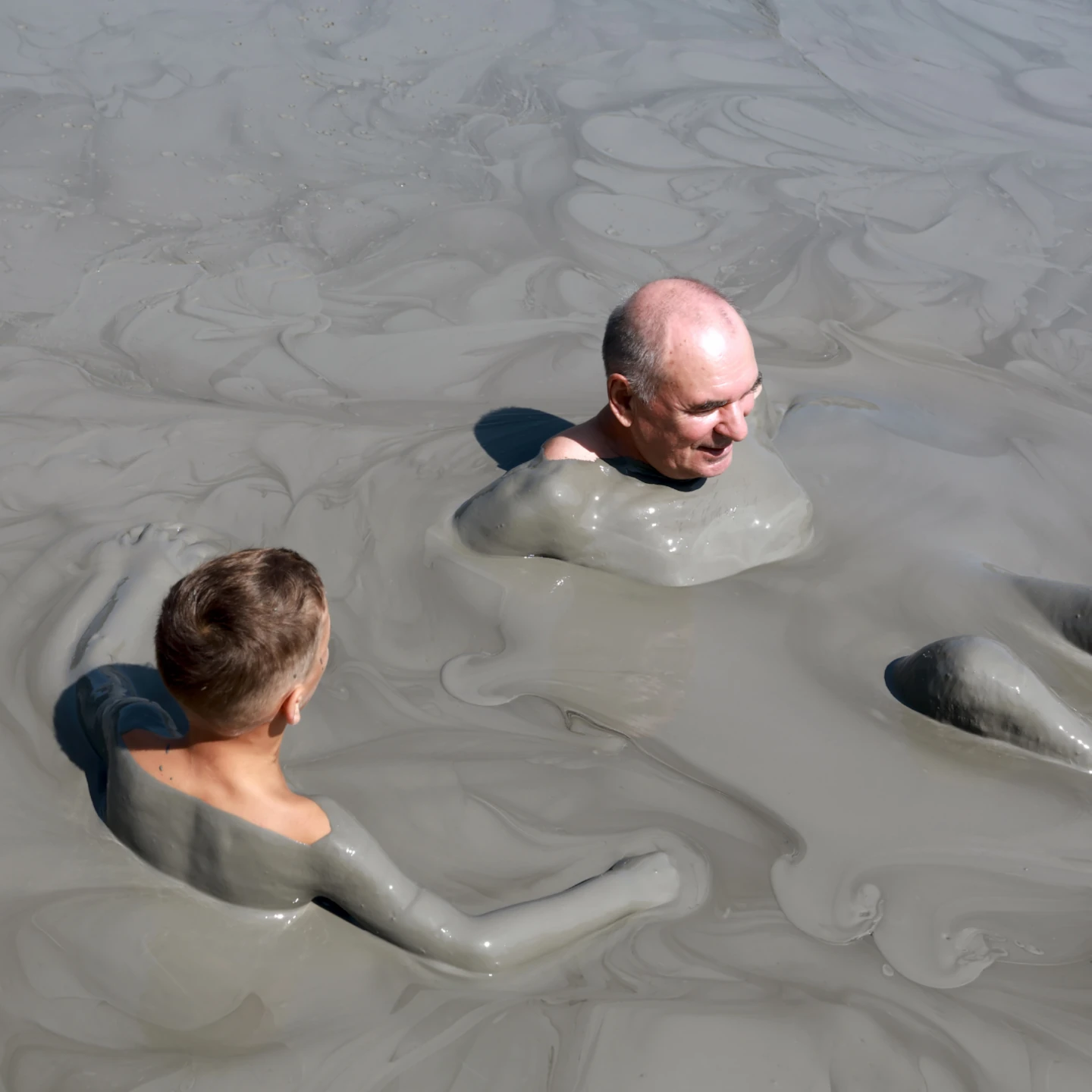 Personas disfrutando de un baño de lodo terapéutico al aire libre