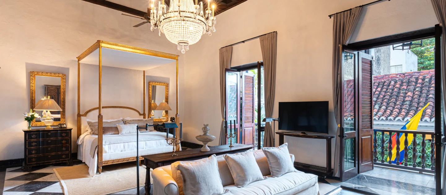 Suite de lujo en Cartagena con cama de dosel dorada, candelabro de cristal y balcón con vista al centro histórico