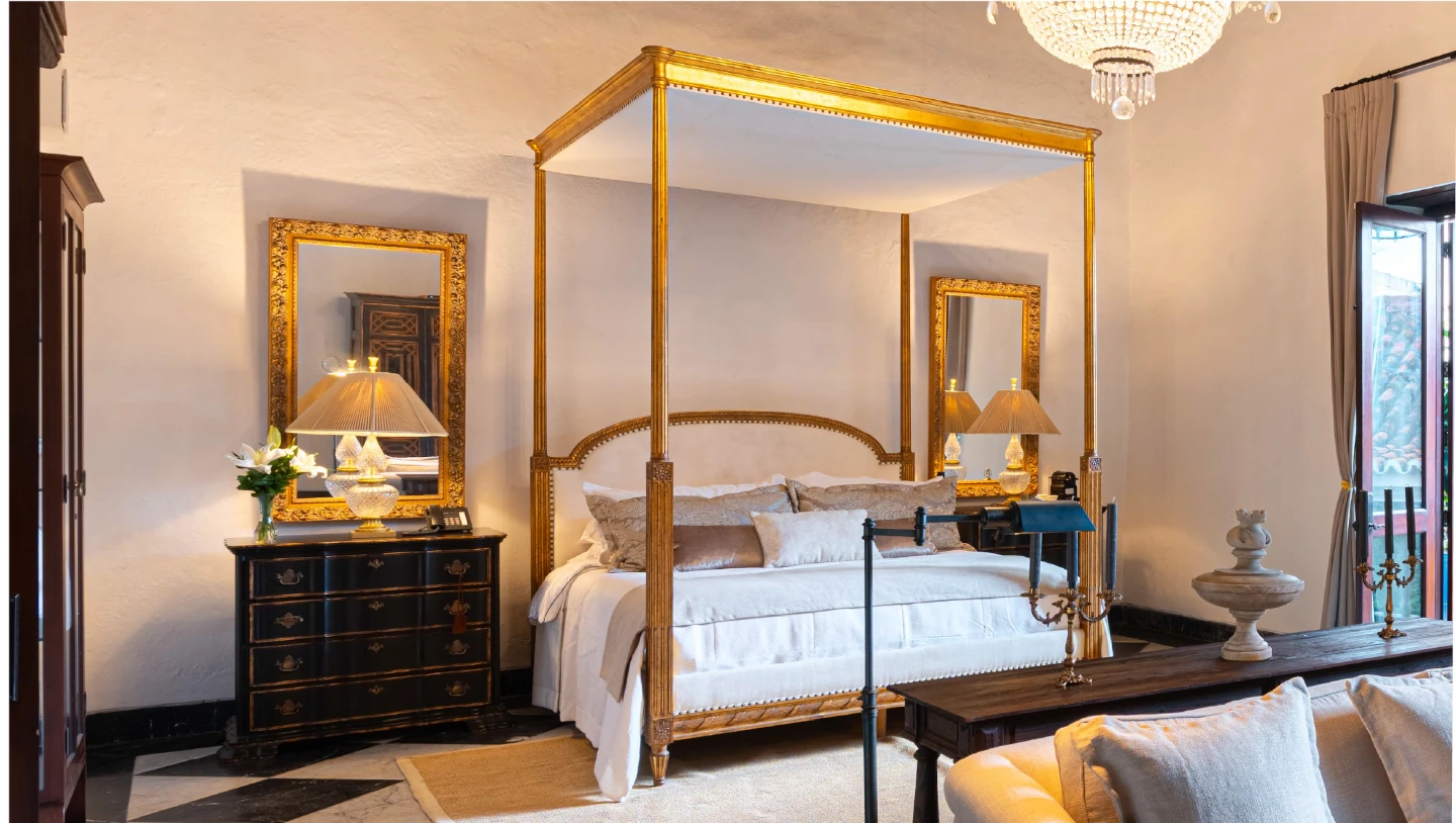 habitación de lujo con cama de dosel dorada, candelabro de cristal y balcón colonial en Cartagena